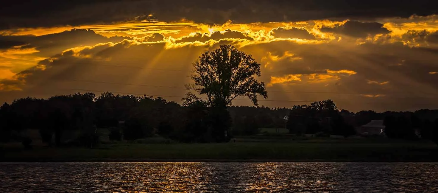 Sonnenstrahlen durchbrechen Wolken über einem Weiher in Mittelfranken bei Sonnenuntergang.
